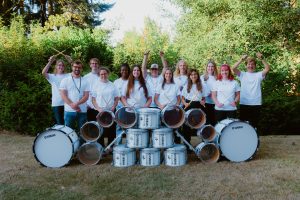 The students of Northwest Drum Line smiling and standing behinds drums on a field.