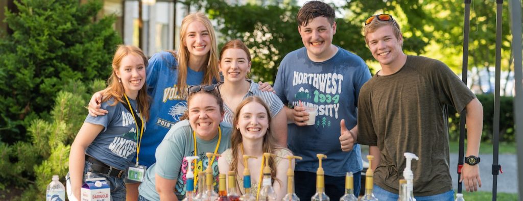 A group of seven smiling college students positioned behind a table with Italian soda ingredients.